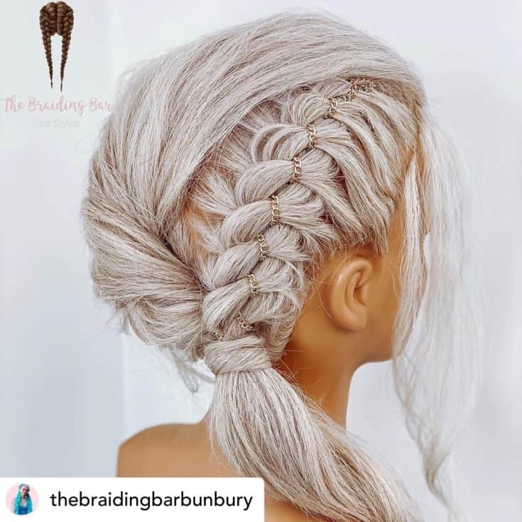 An intricate braid hairstyle with blond hair and small gold rings woven into the plaits, showcased on a mannequin.