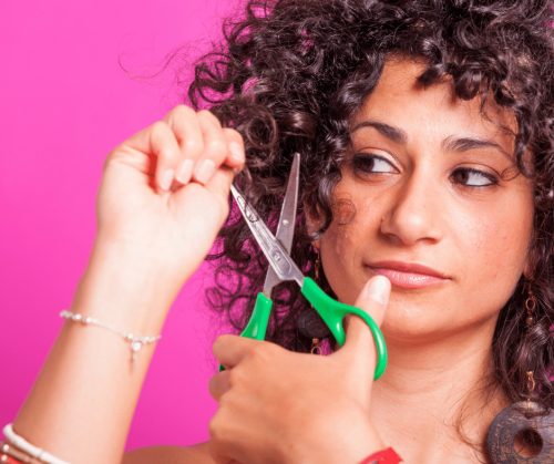 Woman with curly hair, cutting her own hair with scissors.