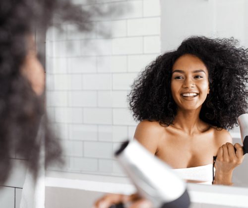 Beautiful African American woman with natural hair blow drying hair.