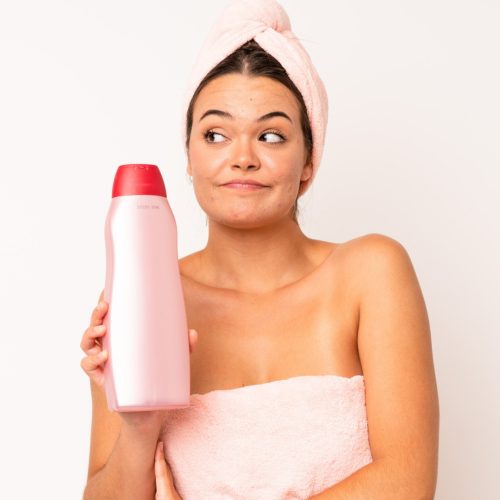 Woman with her hair wrapped in a towel, holding a shampoo bottle in her hand.